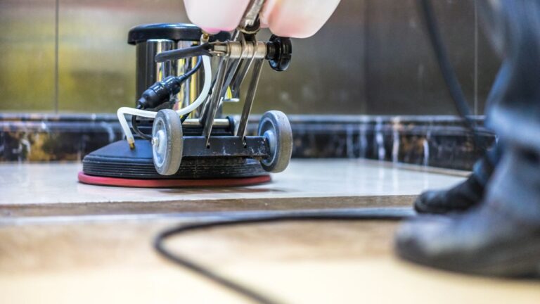 close up of a eletric broom and the feet of a person cleaning the stone floor of a elevator