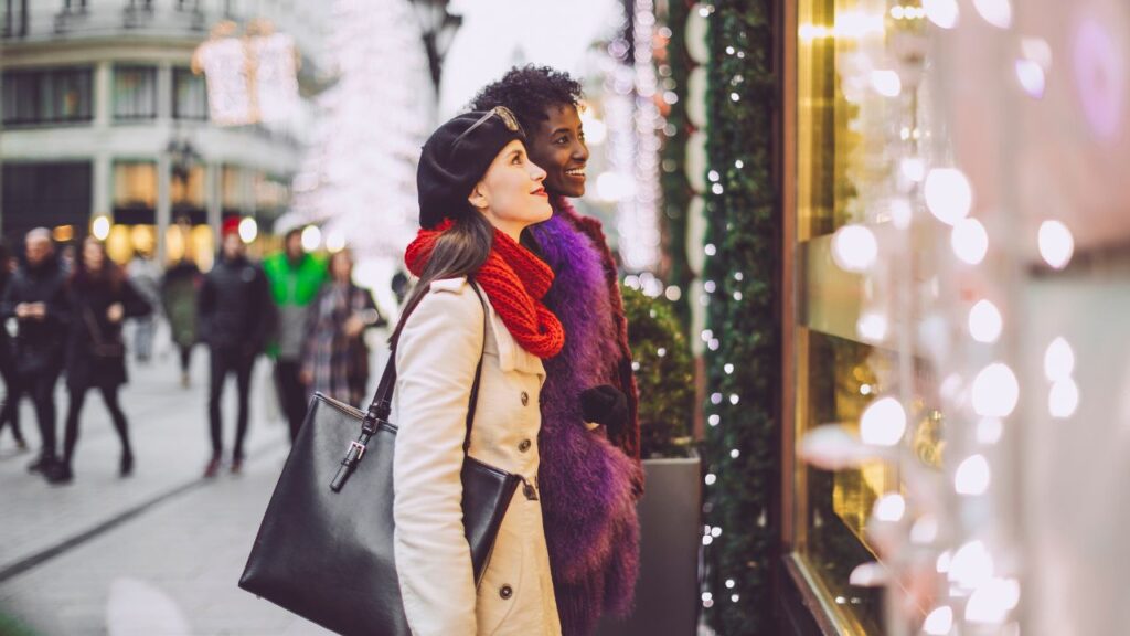 two women dressed for winter staring into a store through the window