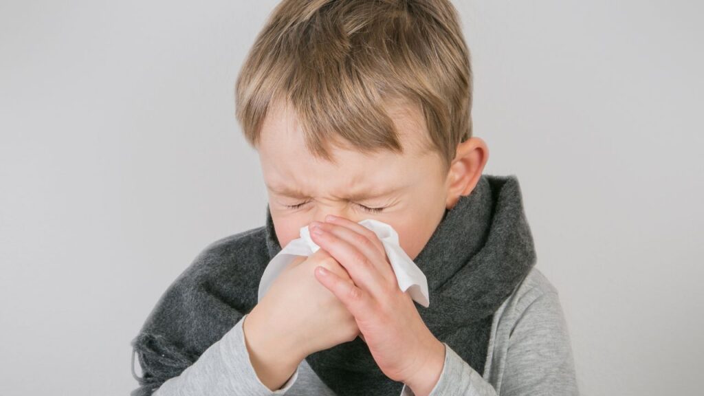 little boy sneezing into tissue