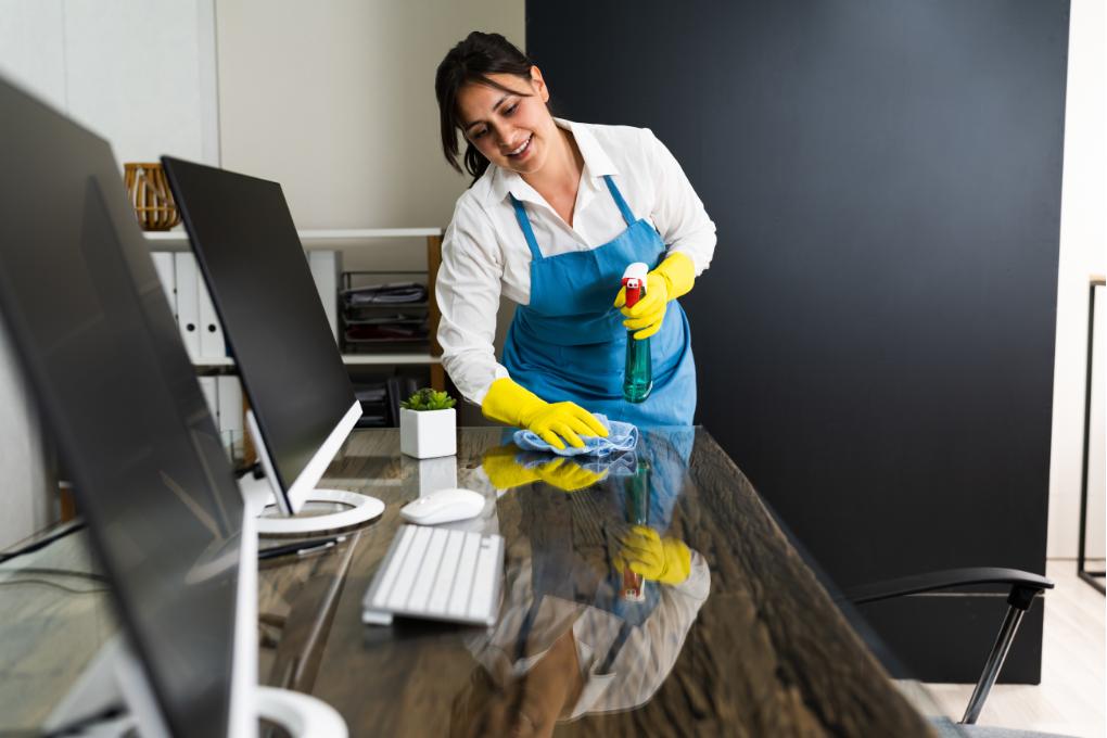 woman cleaning computer desk in office