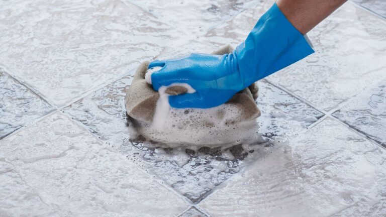gloved-hand-scrubbing-tile-floor-with-soaped-sponge